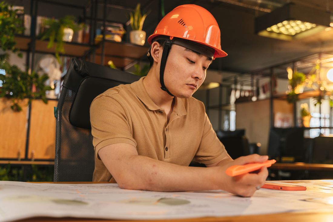 Architect in an orange hard hat reviewing technical drawings at a desk
