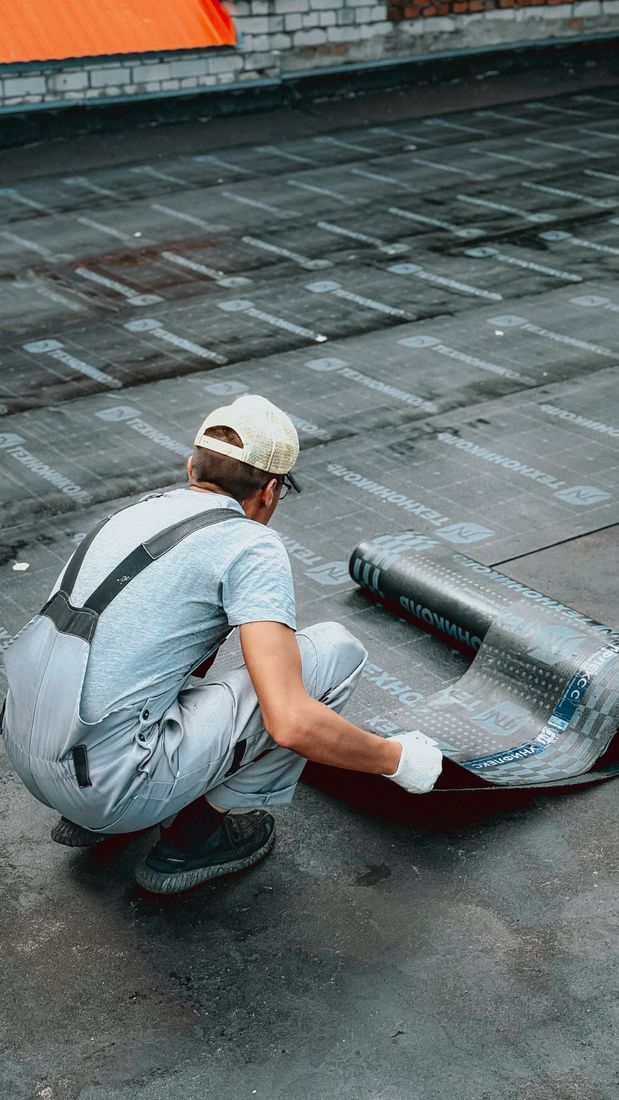 Roofer positioning waterproof membrane on a flat roof